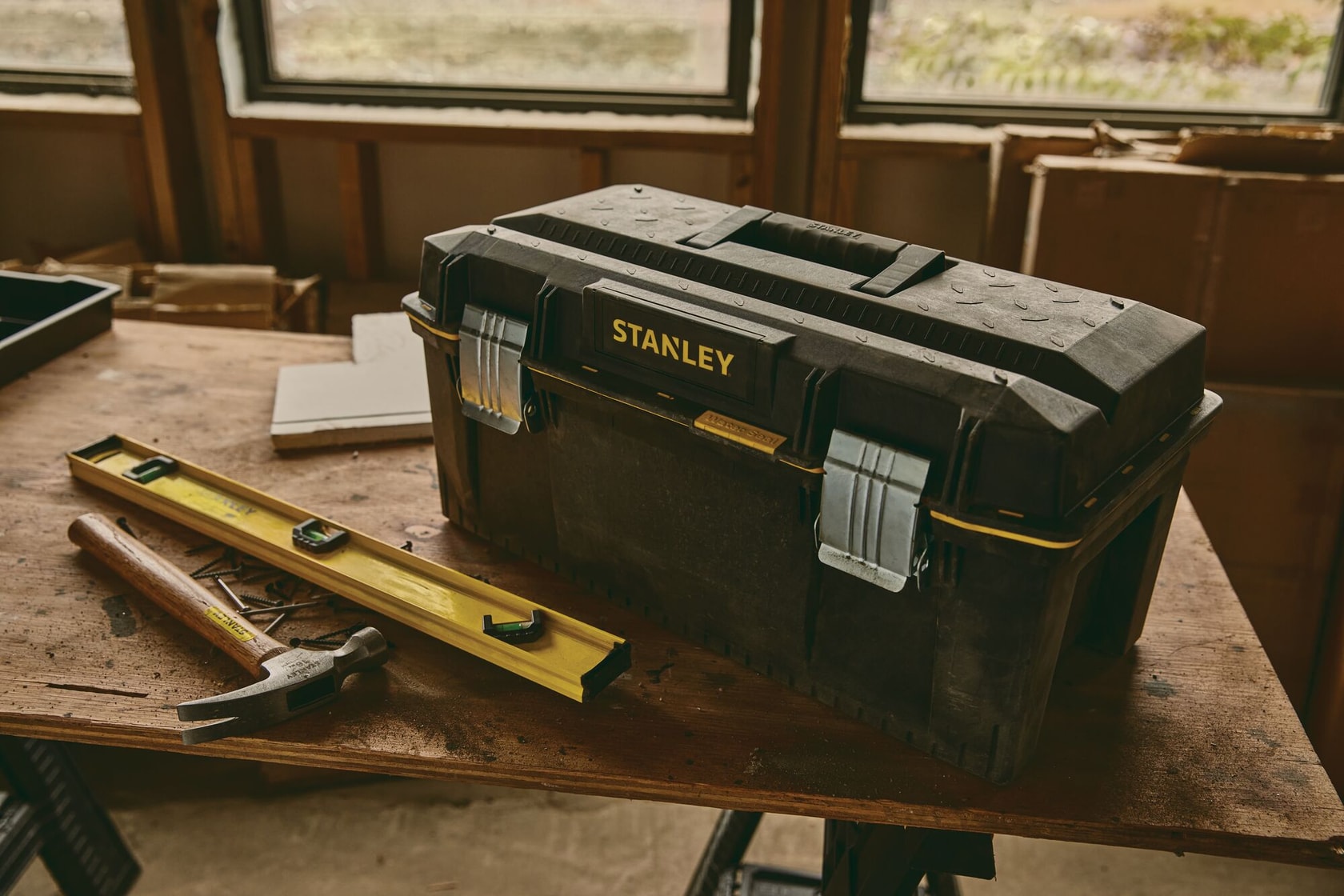 Stanley 023001W toolbox with metal latches on a workbench, hammer and level nearby, workshop setting.